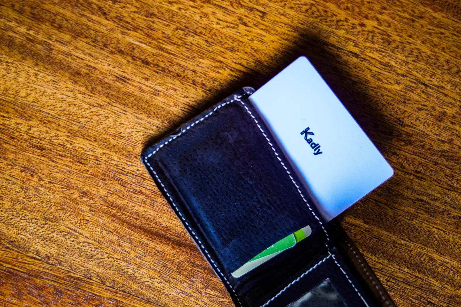 Kadly white NFC business card slid into a leather wallet beside a bank card, replacing a stack of paper cards