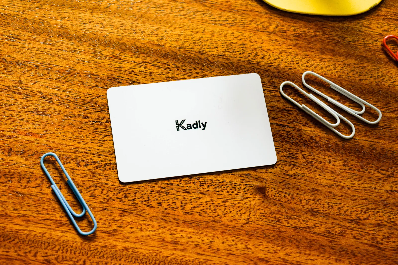 Kadly Classic white NFC business card on a wooden desk with paper clips